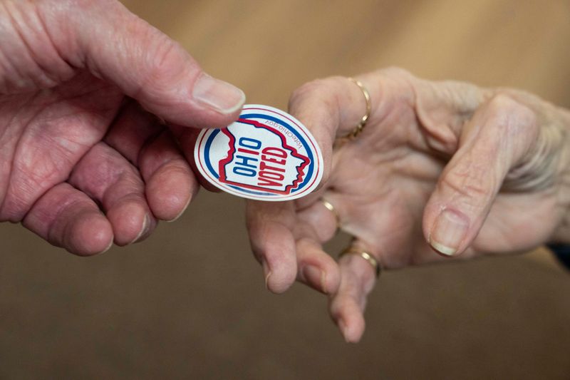 A poll worker hands an “Ohio Voted’ sticker to Robert Jessup, of Lancaster, after he casted his ballot at the Shining Light Community Church for the Fairfield County General Election on Nov. 4. 2025, in Lancaster, Ohio.
