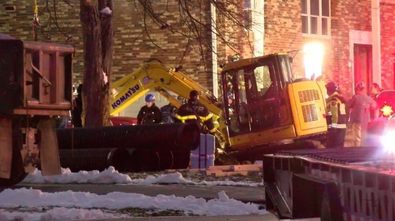 Three men were trapped after the trench collapsed on Dec. 5, 2025. The photo shows the residence, emergency workers, and a Komatsu excavator that was used to dig much of the trench.