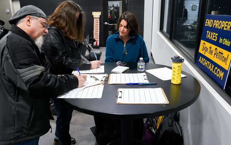 Sarah Wolf, right, collects signatures for a proposed constitutional amendment to eliminate property taxes during an event at Queen City Harley-Davidson in January.