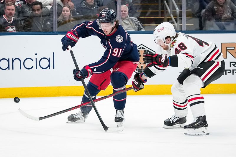 Blue Jackets center Kent Johnson passes around Blackhawks defenseman Matt Grzelcyk on Feb. 4.