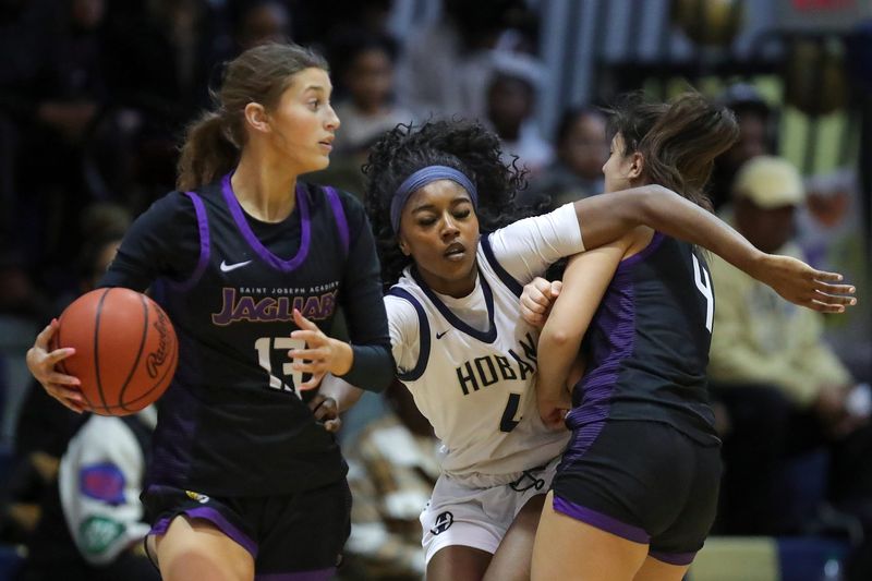 Hoban forward Makenzie Grant, facing, slams into Saint Joseph guard Cameron Croce, right, as forward Sophie Stehlik looks to pass during the first half of a high school basketball game, Feb. 7, 2026, in Akron, Ohio.