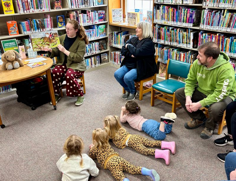 Children gather on the floor and eagerly listen as Rachel Hill, youth services coordinator for the Coshocton County District Library, reads a book during Lapsit storytime at the West Lafayette Branch Library in this Tribune file photo. This regular program and other special events and activities will tie into the annual summer reading program with the theme of Unearth a Story for 2026.