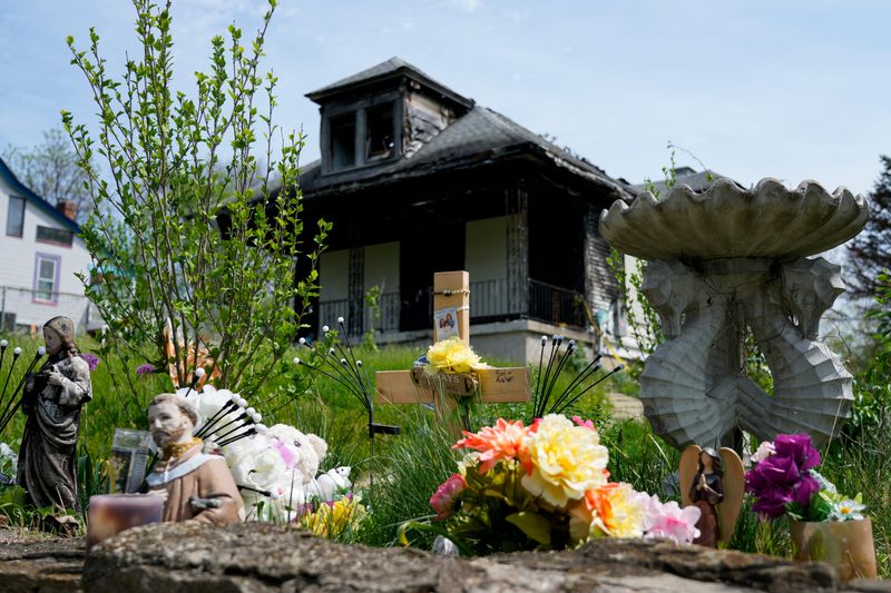 A memorial with flowers, candles and religious statues rests outside the burned remains of 4684 North Edgewood Ave., months after a fire there killed three.
