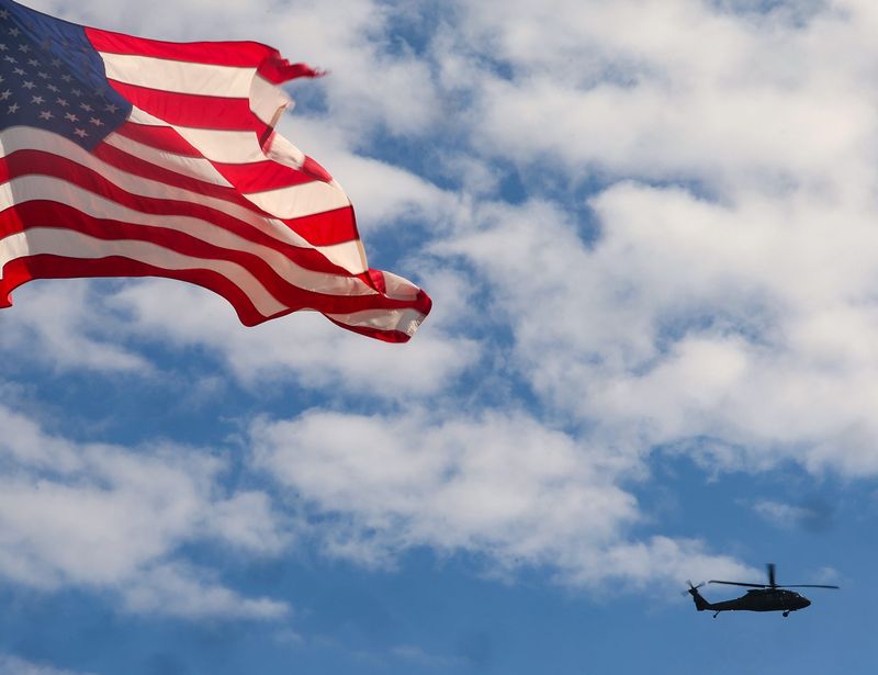 A military helicopter shares the sky with an American flag above Bainbridge High School on Thursday, April 16, 2026.