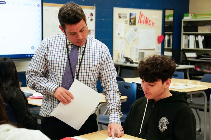 Joel Peck, left, assists Yorvin Paez Suarez, 13, right, with a worksheet during class, Thursday, April 16, 2026, at Pleasant Hill Academy in College Hill. Peck is a CPS teacher who teaches English to immigrant students, mostly Spanish-speaking students.