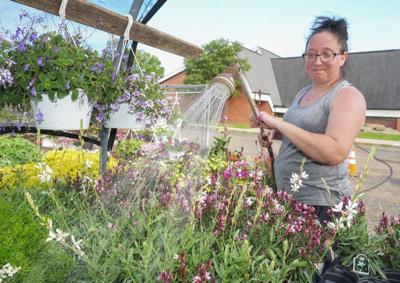 Amanda Kemp waters flowers at Mary Ann’s Flowers in Massillon on a warm spring day.