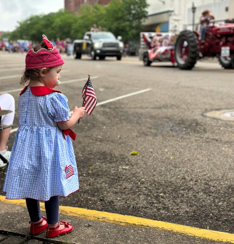 Two-year-old Revie Casey waves a small flag as entries pass her during the 2026 Coshocton County Memorial Day Parade. She's the daughter of Bryan and Karrie Casey of Coshocton. Her great-grandparents Doris and Terry Casey both served during World War II and were at the parade on May 25. Doris served in the mail room at Fort Des Moines, lowa. Terry was a private first class involved with field artillery and destroyers in the European Theatre. He is 100 years old.