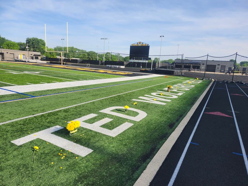 Yellow roses, mums and flower petals are laid amid the name of Ted Wolford Field at Upper Arlington before the Golden Bears boys lacrosse team played New Albany in the Division I, Region 3 final May 29. Wolford, who led UA to 16 state championships, died the previous day at age 66.