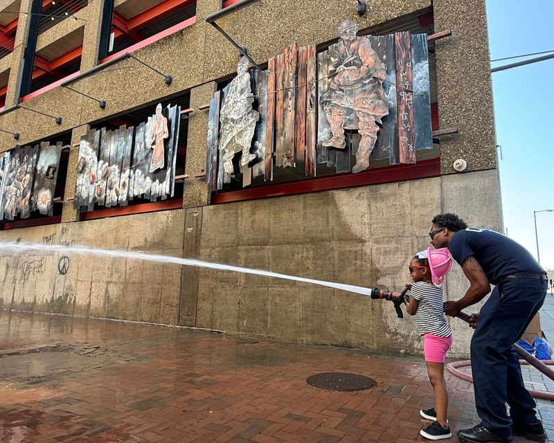 Genesis Davis, 6, of Canton, has fun spraying a hose with a Canton firefighter as part of a downtown event at Centennial Plaza. Pictured in the background is one of the many examples of artwork on display in the Canton Arts District.