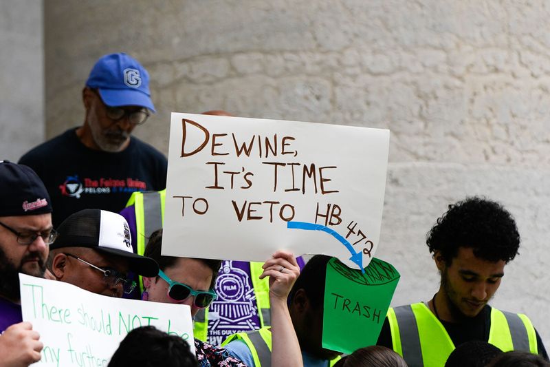 A sign says, “DeWine, it’s time to veto HB 472” protest against House Bill 472” outside the Ohio Statehouse on Wednesday, June 24, 2026 in Columbus, Ohio.