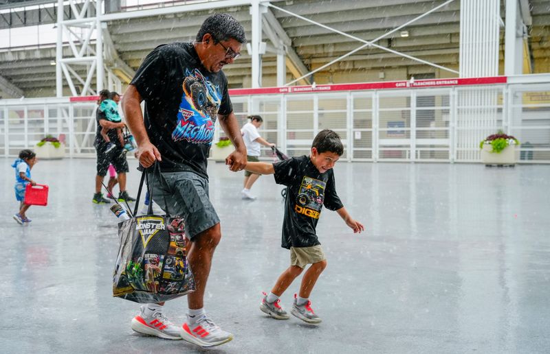 An older Megalodon fan runs with a young JCB DIGatron fan during a heavy rain after the end of Monster Jam’s show at the Heritage Bank Center on Saturday, July 11, 2026.