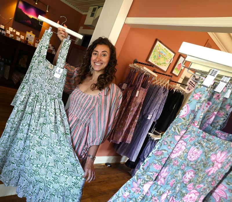 Clarity Cotton owner, founder and designer Jaye Lenchis holds one of her dresses in her New Concord storefront. Each dress is handmade and crafted with a centuries-old method using wooden blocks carved with a template pattern. The block is then used over and over again to stamp the same pattern across the dress. She has about 70 different patterned dresses in her shop and only makes 8 of each to keep the inventory fresh.