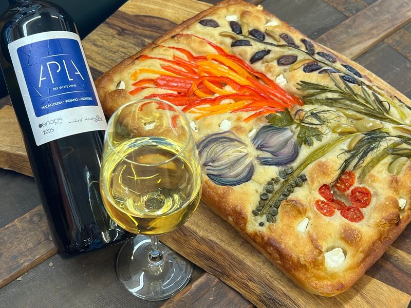 A glass of Apla white blend from Greece pairs perfectly with a floral focaccia bread from Fournos Crafted by Angie. This tasty and beautiful $20 creation can be purchased at Canton Importing every Friday. Photo by Phil Masturzo