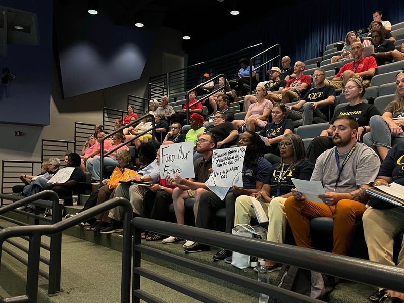 Members of the Cincinnati Federation of Teachers held posters criticizing Cincinnati Public Schools' Board of Education at the Aug. 3 meeting where the board rescinded its earned income tax levy vote from a week prior.