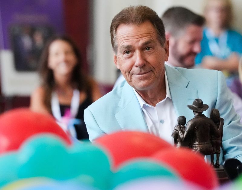 Aug. 4, 2026; Tuscaloosa, AL, USA;  Nick Saban smiles as hold the Lifetime Achievement Award he and Terry Saban are about to present to Stephanie Bryan, Chair and CEO of the Poarch Band of Creek Indians, at the North Zone in Bryant-Denny Stadium for the annual Nick’s Kids Luncheon. More than $775,000 was given to a variety of organizations during the event.