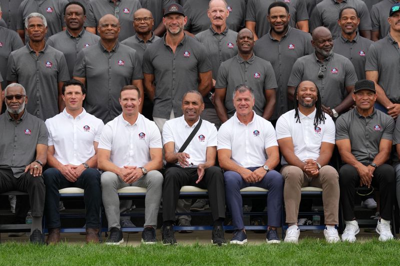 Aug 7, 2026; Canton, OH, USA; Pro Football Hall of Fame Class of 2026 enshrinees Luke Kuechly, Drew Brees, Roger Craig Adam Vinatieri and Larry Fitzgerald pose with past inductees at the Pro Football Hall of Fame. Mandatory Credit: Kirby Lee-Imagn Images