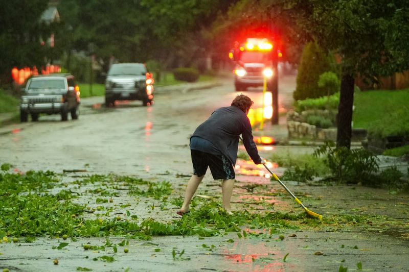 Griffin Herriott-McGown sweeps branches and leaves off of Calumet Street as Clintonville residents clean up storm damage after a severe thunderstorm blew through Columbus on Aug. 11, 2026. Power was out for many residents and many trees were down.