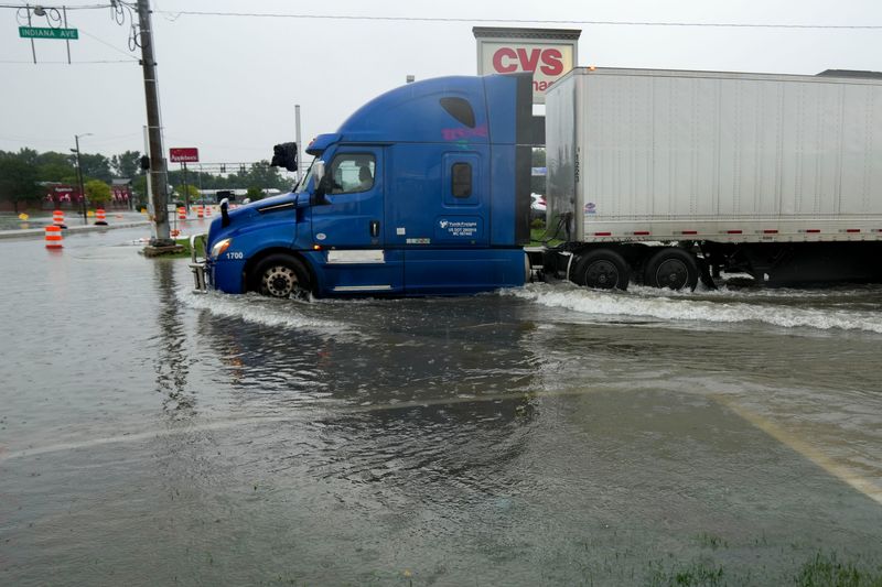 A truck passes through water following flooding Wednesday, Aug. 12, 2026, at the intersection of Indiana Avenue and south Memorial Drive in New Castle, Ind.