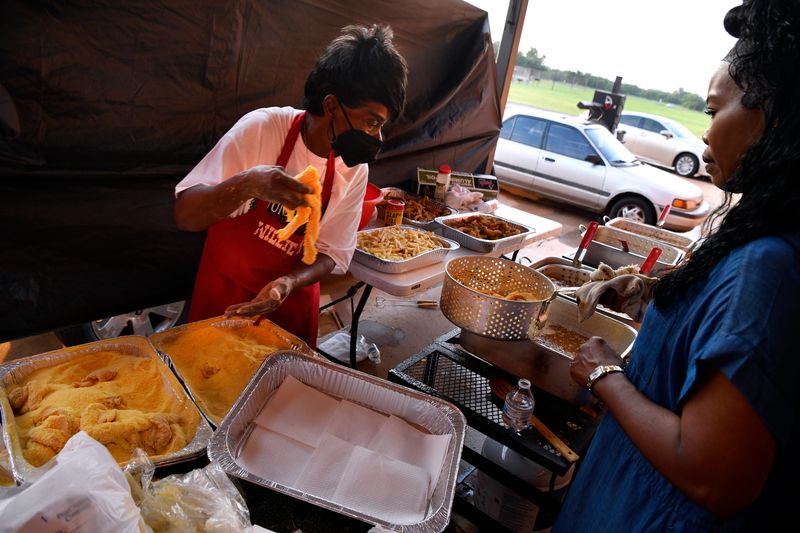 Audrey Clayton (left) batters catfish as Jackie Lowry holds the steel basket at the June 17, 2023, Juneteenth Fish Fry at Stevenson Park.