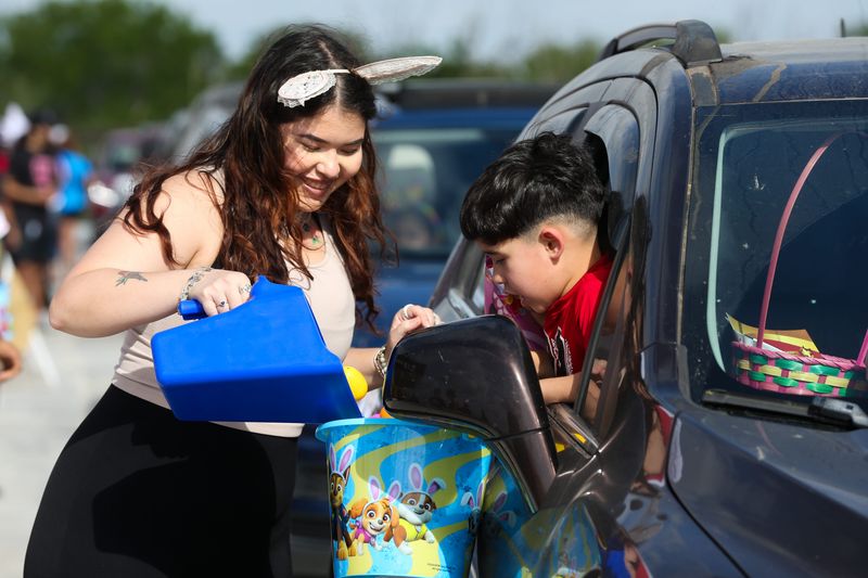 Hot Z95 on-air personality Victoria De Leon pours Easter eggs into a child's basket at Hot Z95's annual Easter Egg-stravaganza Drive-thru at the School of Science and Technology on March 30, 2024.