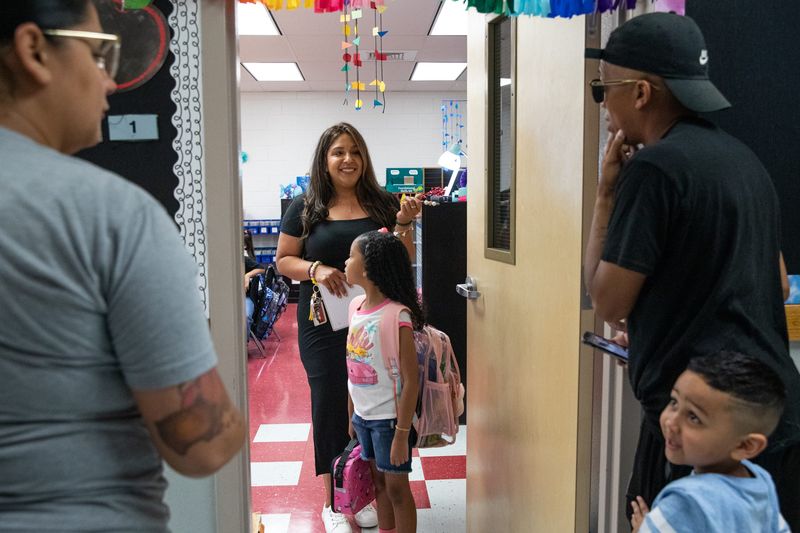 Second grade teacher Monica Pena speaks to parents Tim Taylor and Brittney Martinez in the hallway on the first day of school at West Oso Elementary on Tuesday, Aug. 13, 2023, in Corpus Christi, Texas. Their daughter Brailey Taylor stands in the doorway of her news classroom while son Lennox Taylor stands behind is father.