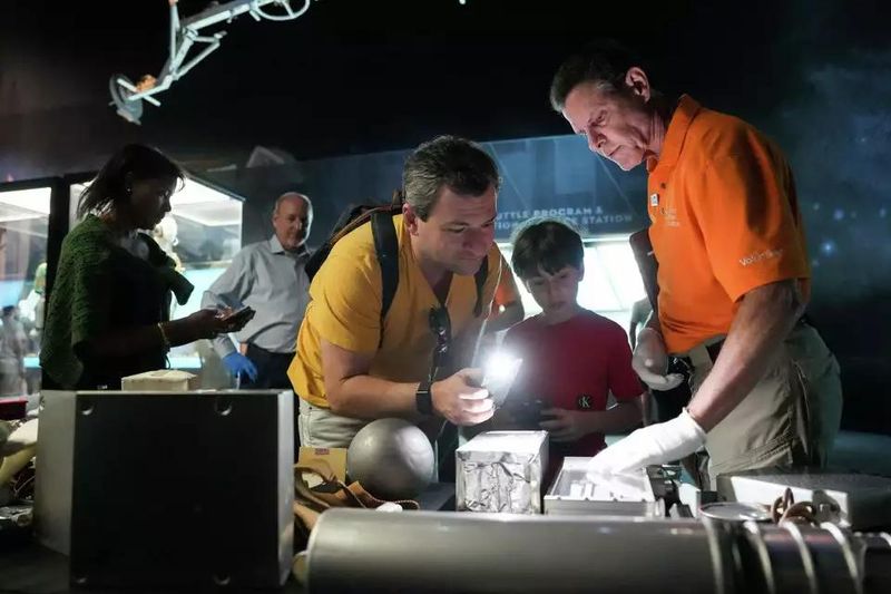Fabio Vitiritti, left, and his son Thomas Vitiritti, 8, listen as volunteer Marc deChellis tells them about Skylab-era items found in an old trainer mockup at Space Center Houston.