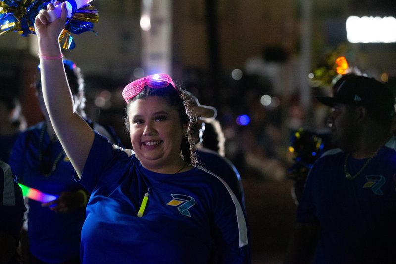 A marcher with Rally Credit Union waves to people at the annual Buc Days Rally Night Parade on Schatzell Street in downtown Corpus Christi on April 26, 2025.