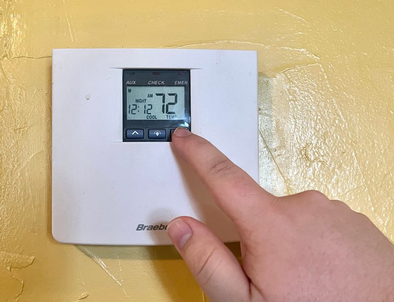A man adjusts the temperature on the thermostat, turning the temperature down.