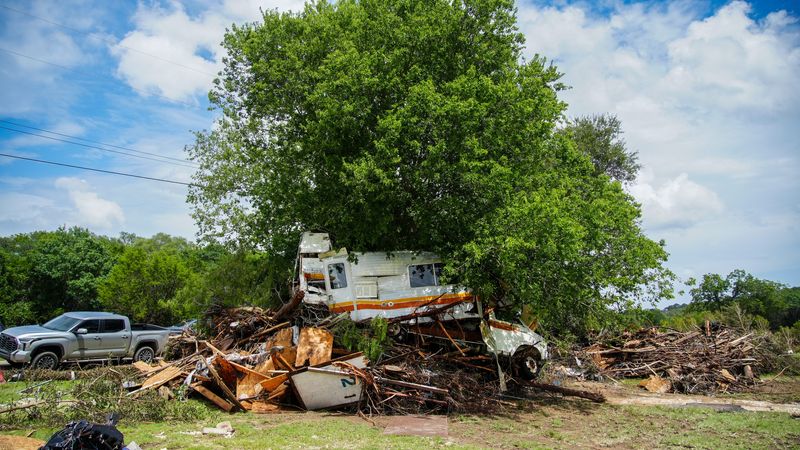 Wrecked vehicles remain submerged in a tree as volunteers work to clean up and recover belongings on July 7, 2025, after a weekend flash flood devastated homes in Leander, Texas.