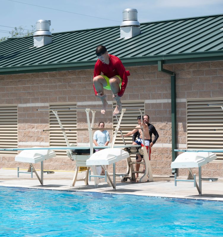 A jumper launches into a cannonball from the diving board as onlookers watch from the pool deck at the Canyon Aquatic Park.