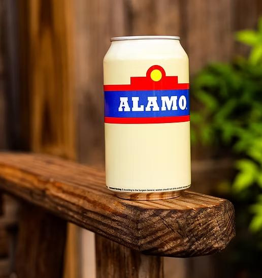The American Style Lager, created by ALAMO Beer Company, comes its iconic can, featuring a red, white & blue "Alamo" logo and beige background.