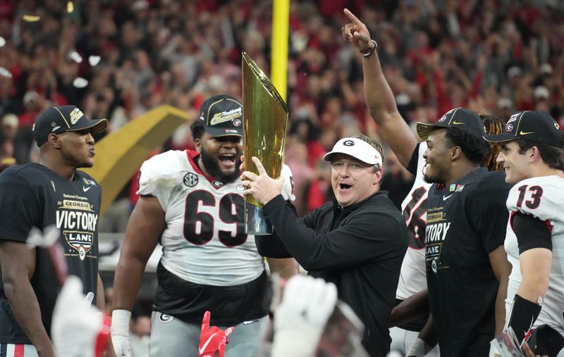 Jan 10, 2022; Indianapolis, IN, USA; Georgia coach Kirby Smart holds the National Championship trophy as offensive lineman Jamaree Salyer (69), defensive back Lewis Cine (16), quarterback Stetson Bennett (13) celebrate after defeating Alabama for national championship.
