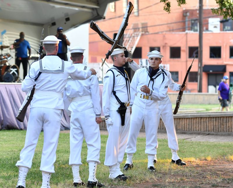Airman Cooper Hollon (left), tosses a standard 1903 Springfield rifle with a 10-inch fixed bayonet to Seaman Alexzander Harris during the U.S. Navy Ceremonial Guard performance at the city of Wichita Falls Outdoor Concert Series at Bud Daniel Park on Tuesday, Sep. 16, 2025. Hollon is an aviation structural mechanic from La Crescent, Minnesota, and Harris is a master-at-arms from Van, Texas. Sailors from the elite unit are performing routines at events during Navy Week in Wichita Falls.