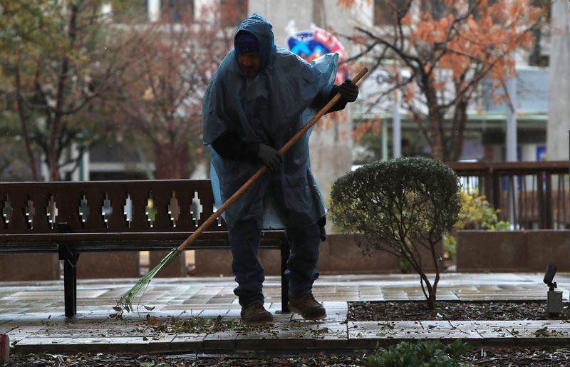 A city employee wearing a rain poncho sweeps leaves at San Jacinto Plaza in El Paso, Texas, on Friday as intermittent rain falls and early‑morning temperatures between 41 and 45 degrees Fahrenheit leave the area feeling sharply colder.