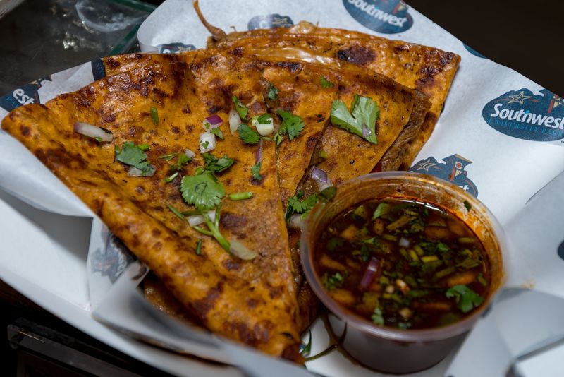 A quesabirria quesadilla with a flour tortilla filled with shredded brisket, melted Monterey Jack cheese, cilantro and diced onions, griddled until golden and served with consommé for dipping, is prepared during a food tasting event for the El Paso Chihuahuas and El Paso Locomotive FC home games at Southwest University Park on Wednesday, Feb. 25, 2026, in El Paso, Texas.