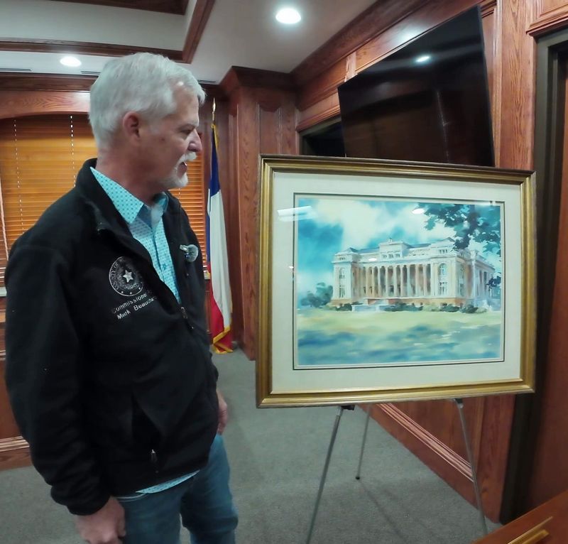 Wichita County Commissioner Mark Beauchamp displays one of 12 paintings of Wichita County historic scenes on Wednesday to soon be displayed in the courthouse.