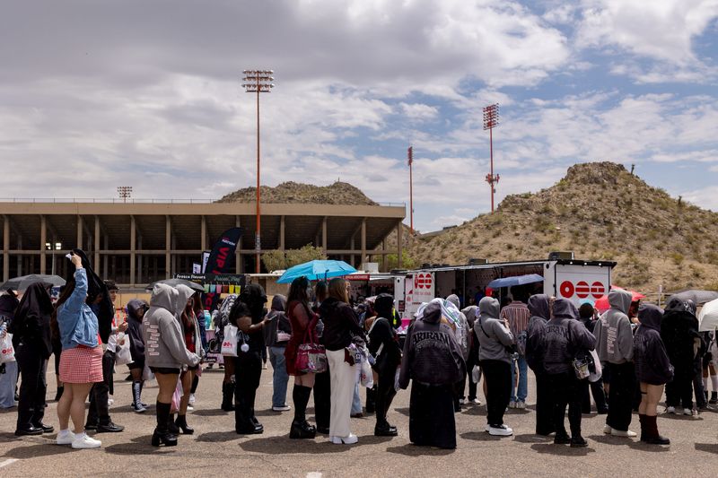 Fans gather under umbrellas and cover up as rain begins outside the Sun Bowl in El Paso, Texas, on Saturday, May 2, 2026, before the first concert.