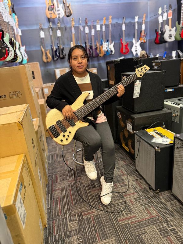 Andrea Pedro Francisco poses with a bass guitar in a music shop