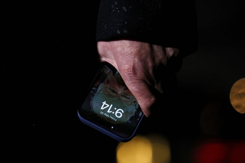 FILE PHOTO: U.S. President Donald Trump holds a mobile phone with his image on it, after his return from Pennsylvania, at Joint Base Andrews, Maryland, U.S., May 30, 2025. REUTERS/Leah Millis/ File Photo