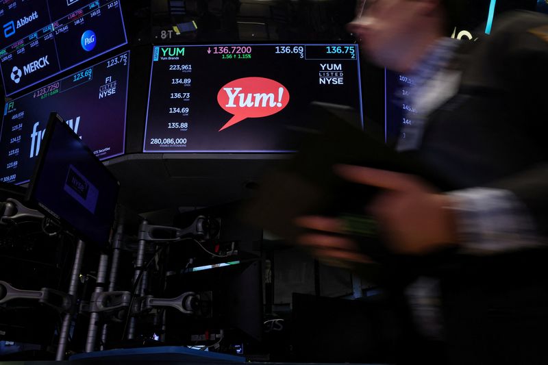 FILE PHOTO: The Yum brand logo and trading information are displayed on a screen as a trader passes by on the floor of the New York Stock Exchange (NYSE) in New York City, U.S., June 29, 2023.  REUTERS/Brendan McDermid/ File Photo