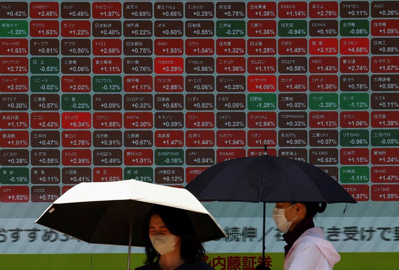 FILE PHOTO: Women holding umbrellas stand in front of a stock quotation board outside a brokerage in Tokyo, Japan June 30, 2025. REUTERS/Issei Kato/File Photo