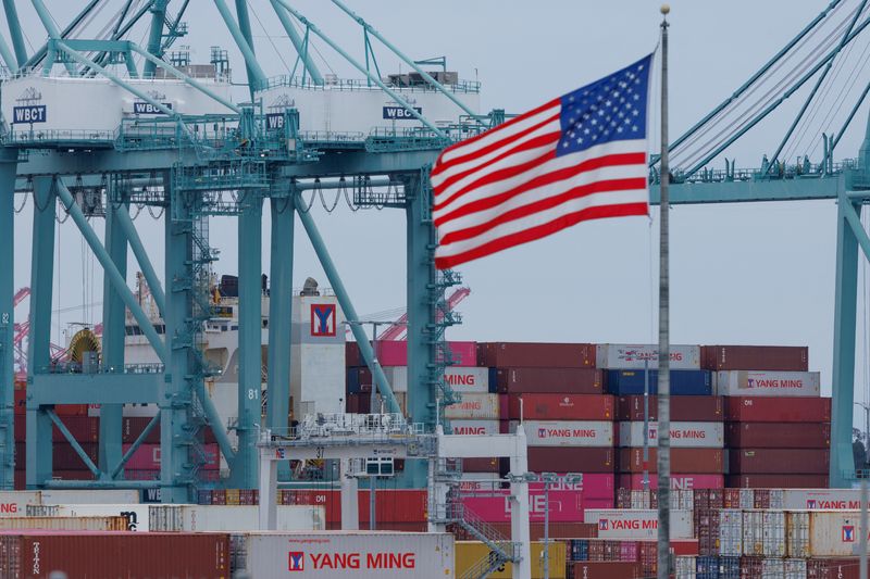 FILE PHOTO: A U.S. flag flutters near shipping containers as a ship is unloaded at the Port of Los Angeles, in San Pedro, California, U.S., May 1, 2025. REUTERS/Mike Blake/ File Photo