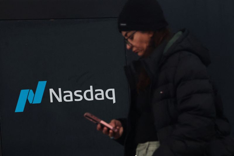 FILE PHOTO: A woman looks at her phone as she walks outside the Nasdaq Marketsite in New York City, U.S., April 3, 2025.  REUTERS/Brendan McDermid/File Photo