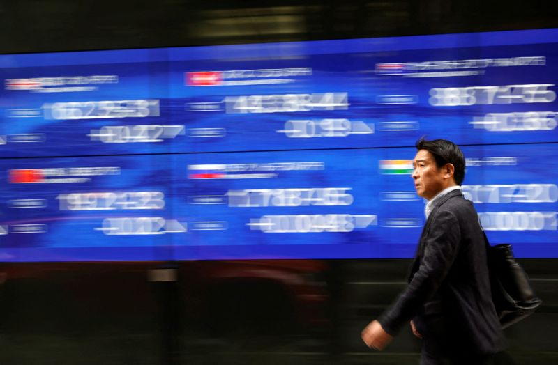 A passerby walks past an electric monitor displaying various countries' stock price index outside a bank in Tokyo, Japan, March 22, 2023. REUTERS/Issei Kato