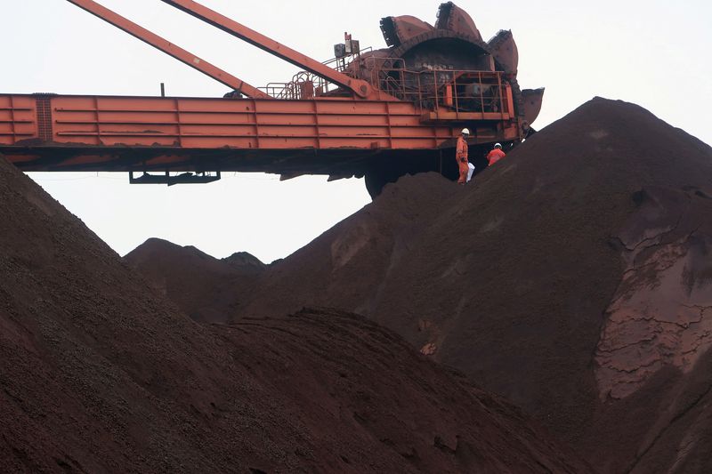 FILE PHOTO: Workers are seen on the top of an iron ore pile as a machine works on blending the iron ore, at Dalian Port, Liaoning province, China September 21, 2018. Picture taken September 21, 2018. REUTERS/Muyu Xu/File Photo