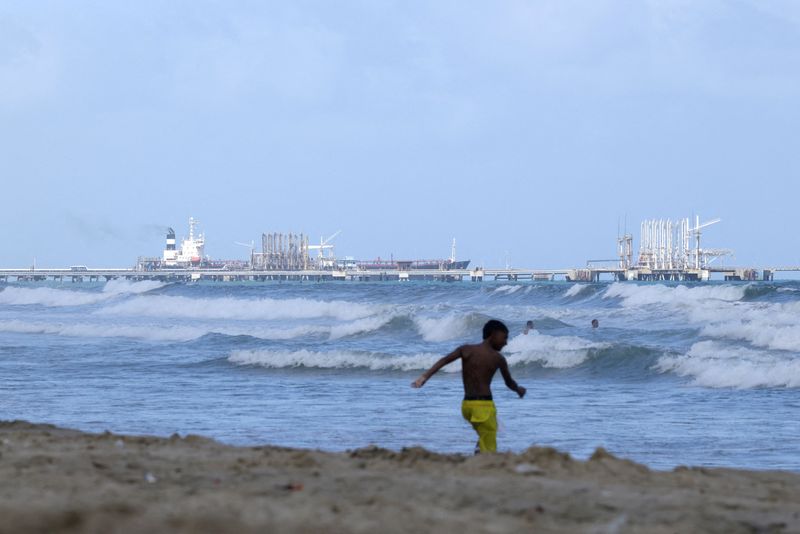 FILE PHOTO: People enjoy the ocean as an oil tanker is anchored near the El Palito refinery of Venezuelan state oil company PDVSA, after the National Assembly approved a major reform of the country's main oil law, in Puerto Cabello, Venezuela, January 27, 2026. REUTERS/Gaby Oraa/File Photo