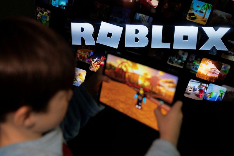 FILE PHOTO: A boy poses for a photo while holding a game pad in front of a screen displaying the logo of the U.S. children's gaming platform Roblox, in this illustration taken December 8, 2025. REUTERS/Ramil Sitdikov/Illustration/File Photo
