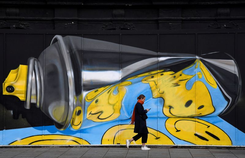 A woman views her phone as she walks past street art on a wall in London, Britain, December 18, 2019. REUTERS/Toby Melville