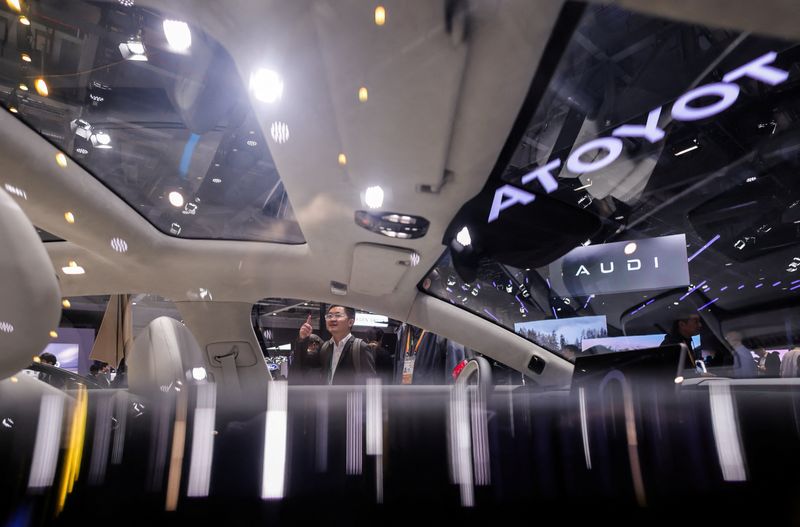 A man gestures as he is seen through the window of a Toyota car with company logo reflected on another window of the car, at the company’s booth at the 8th China International Import Expo (CIIE) in Shanghai, China, November 6, 2025.REUTERS/Maxim Shemetov
