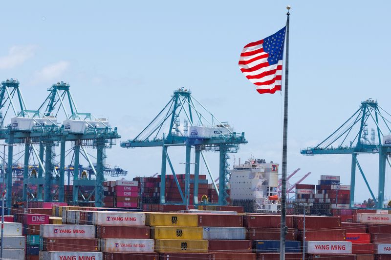 FILE PHOTO: An American flag flutters over a ship and shipping containers at the Port of Los Angeles, in San Pedro California, U.S., May 13, 2025. REUTERS/Mike Blake/File Photo